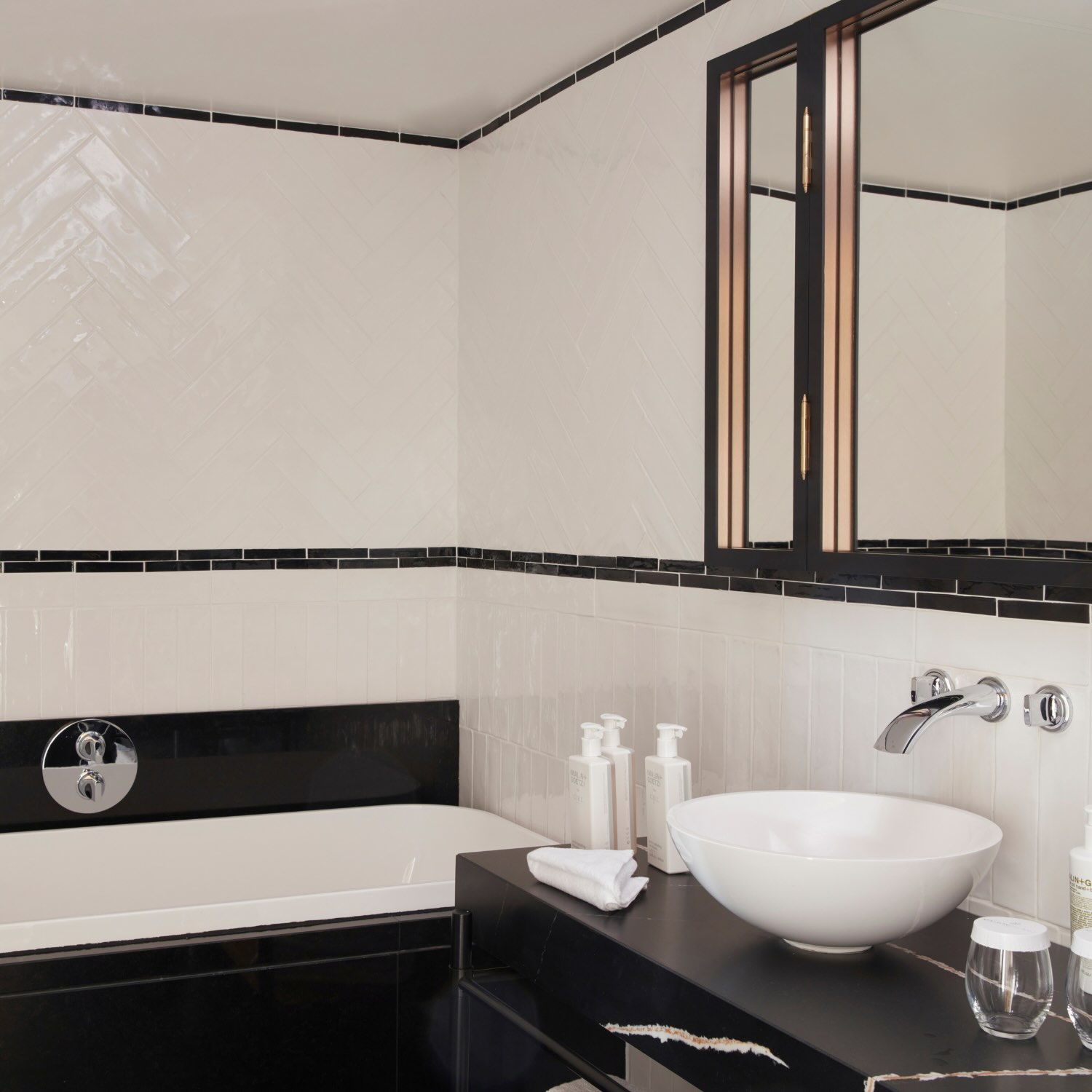 a bathroom vanity with black and white tile and a white bowl sink next to a bathtub