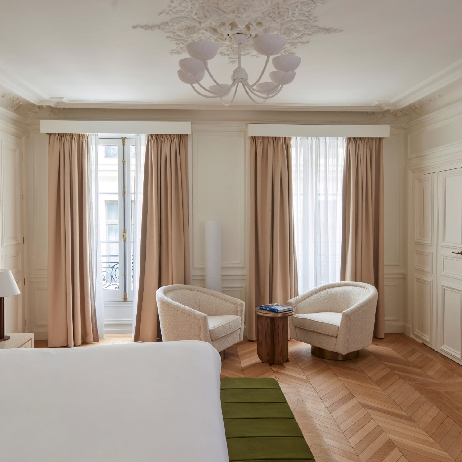 an elegant guestroom with a green bench in front of the bed and seating area in front of the windows