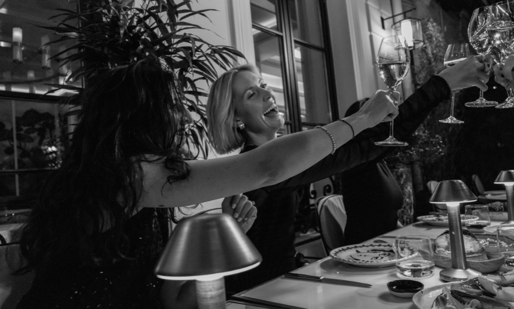 a black and white image of two women gathering and clinking their glasses