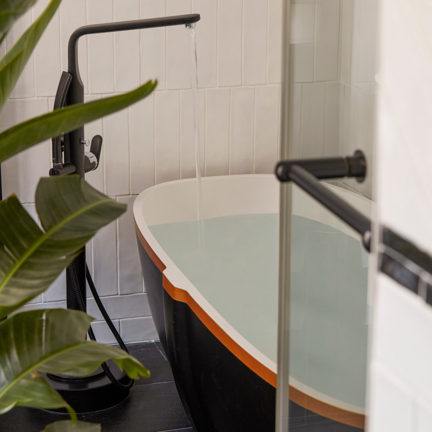 a stand alone black bathtub against white tile 