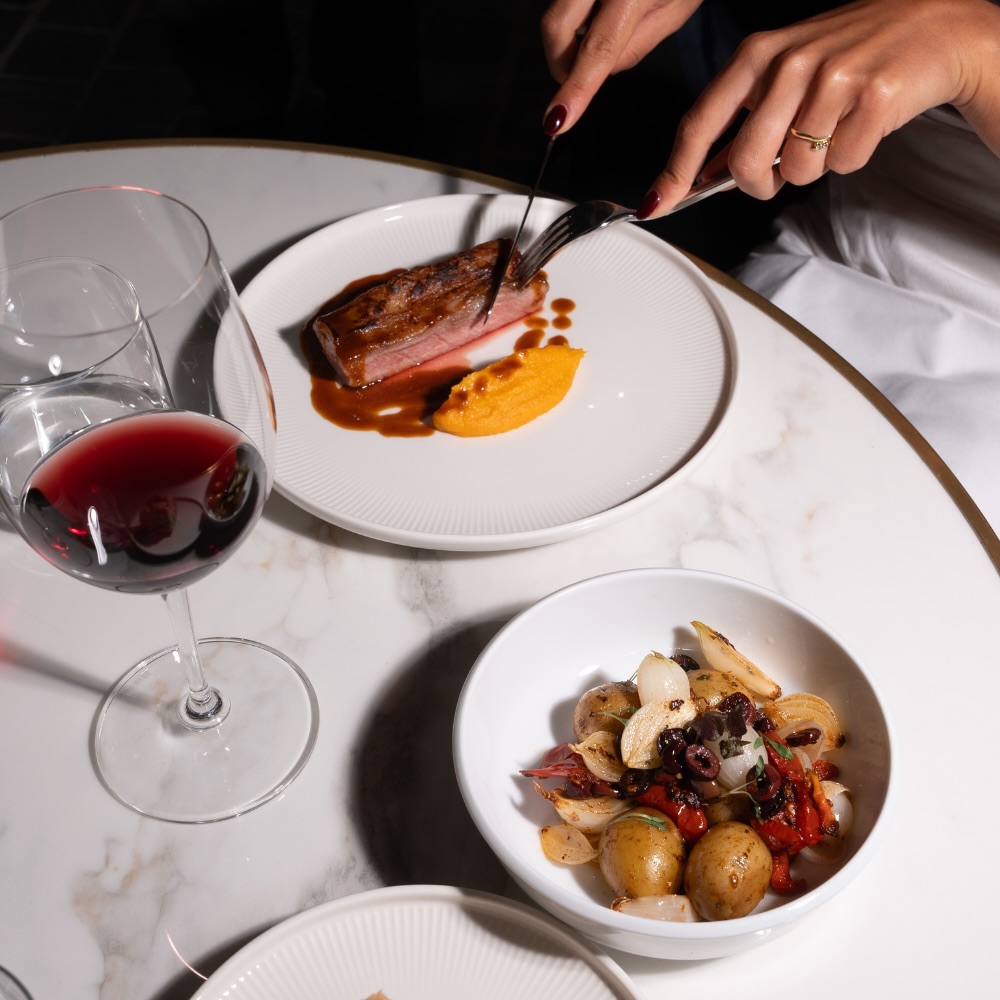 someone dining and eating the steak dish with wine and other dishes on the table