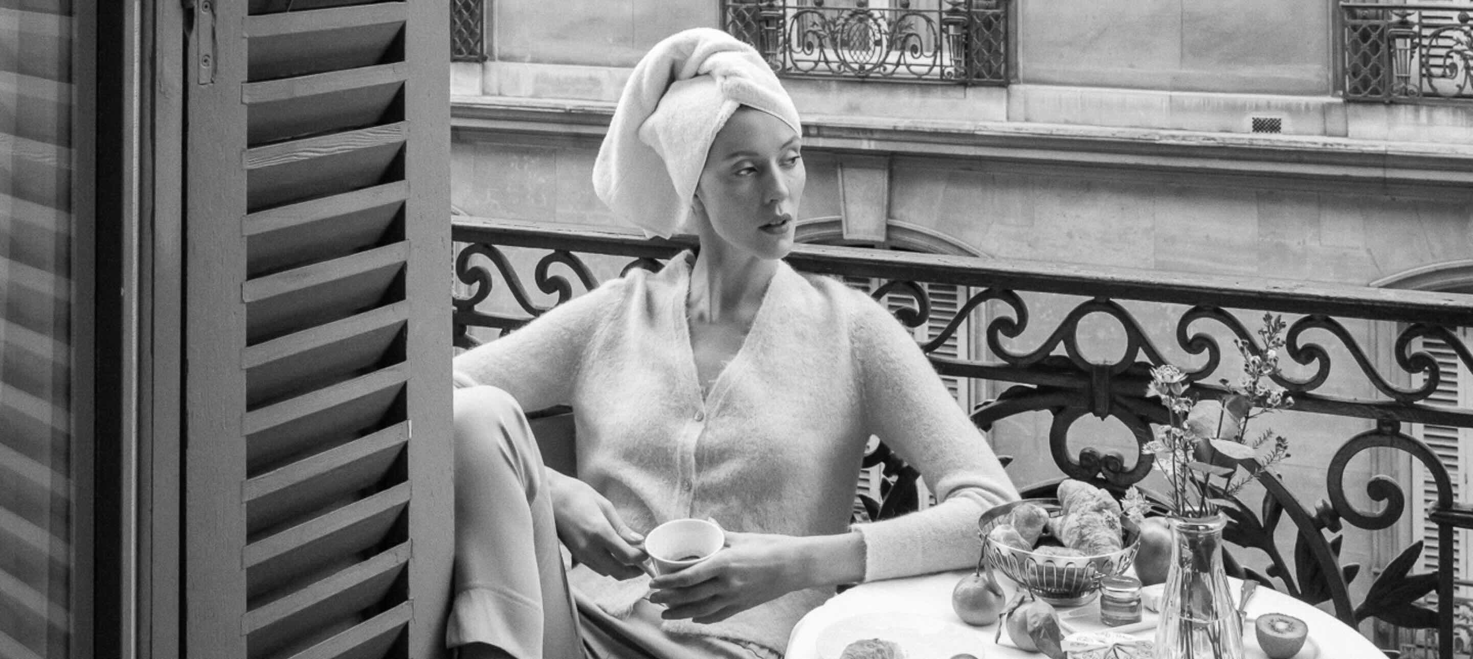 a black and white image of a woman sitting on a terrace of maison delano paris with a towel on her head