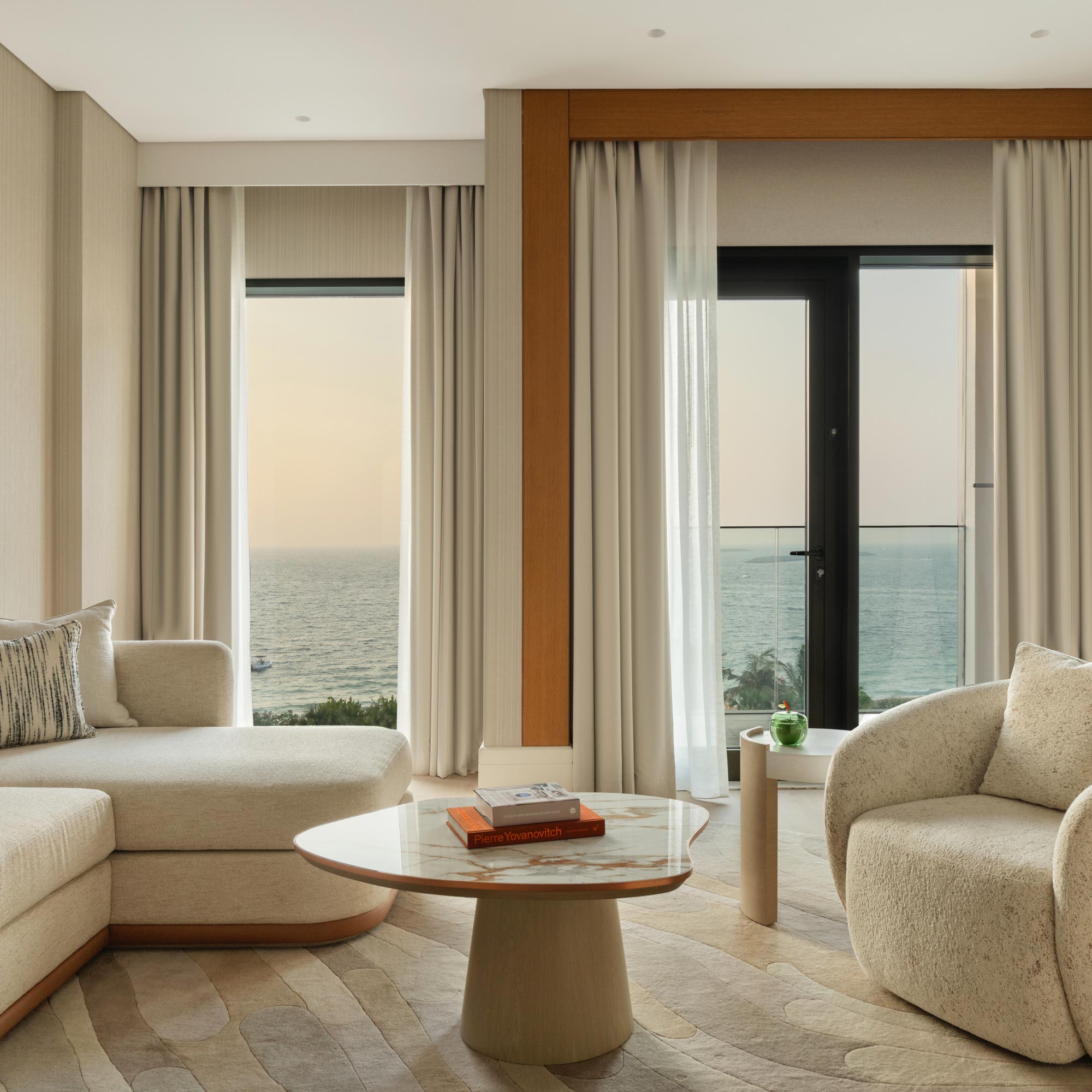 a living space with a white couch and white chair around a coffee table and views of the sea from the windows