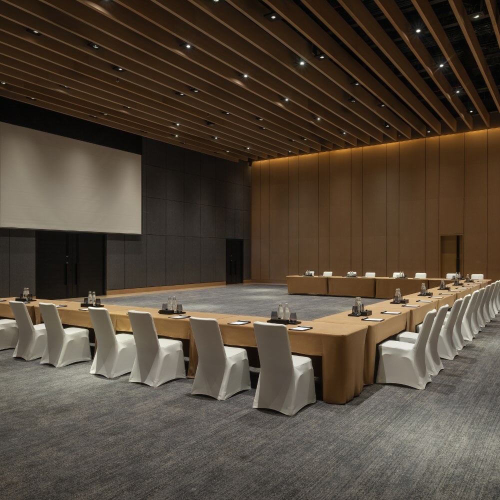 a large convention room with a u-shape table facing a large projector screen.