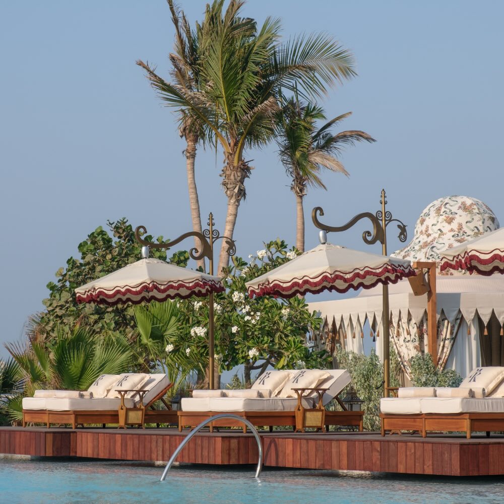 pool side lounge chairs with white and red umbrellas under the palm trees