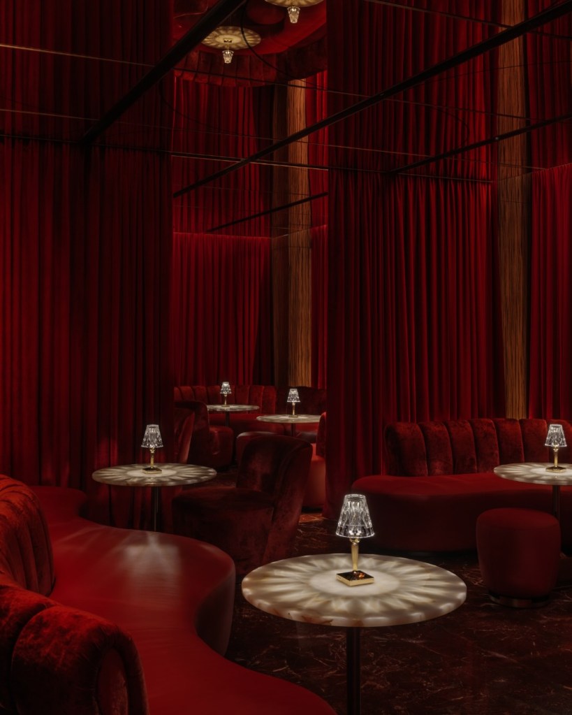 circular red velvet booths with small tables and red wallks