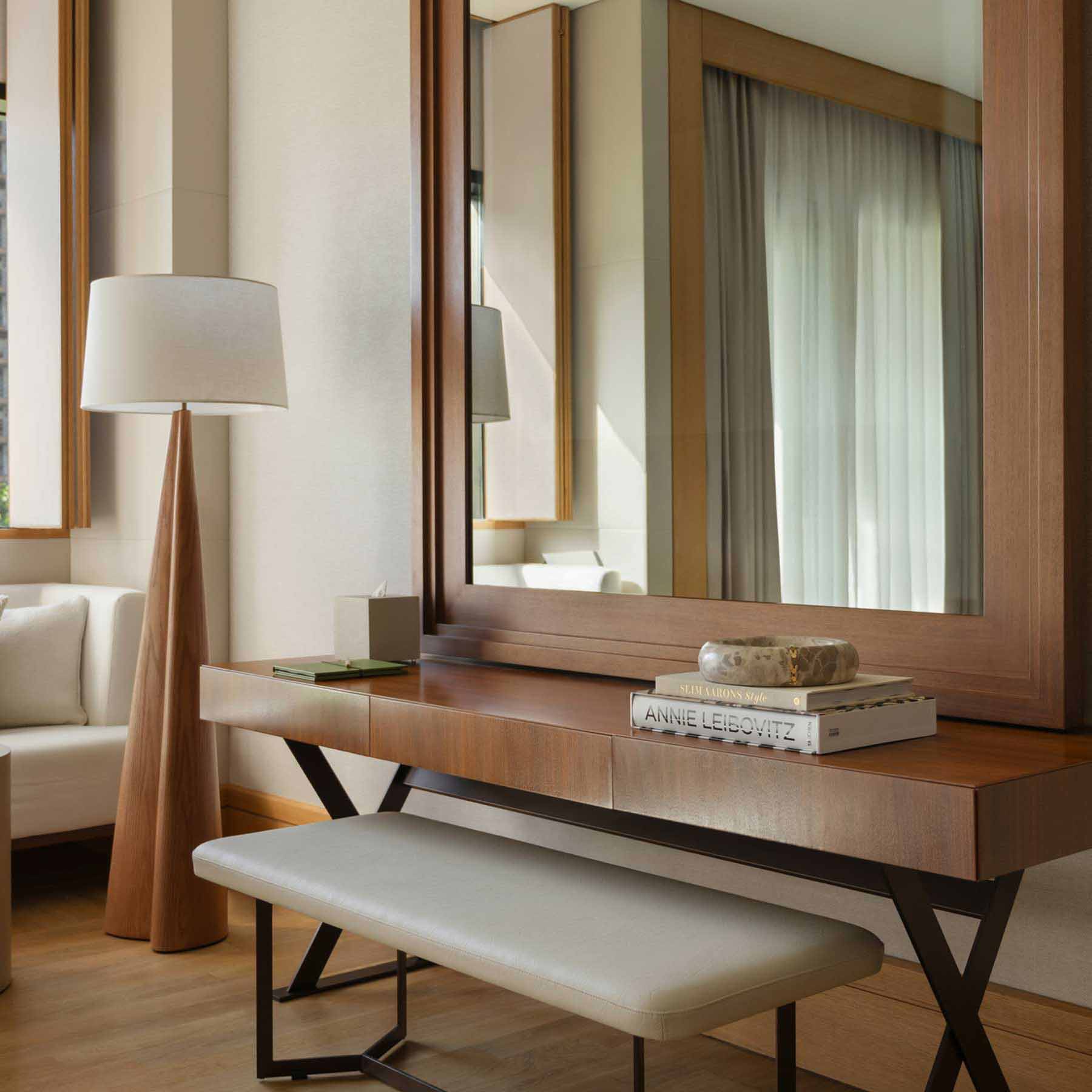 a desk facing a large wall mirror with a bench tucked underneath