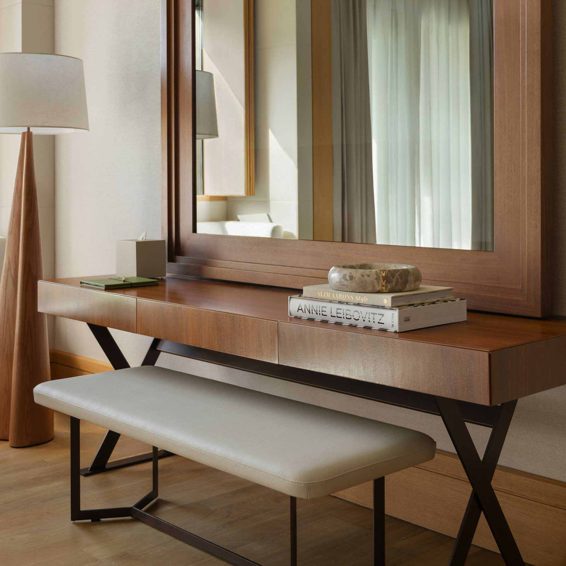 a desk facing a large wall mirror with a bench tucked underneath