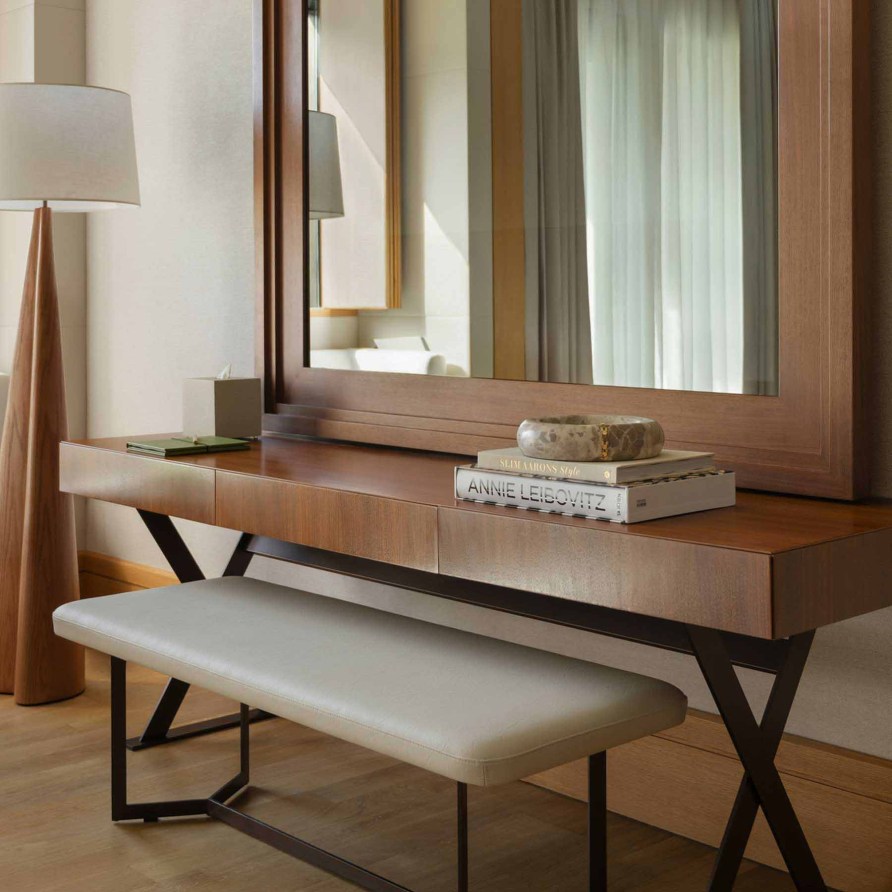 a desk facing a large wall mirror with a bench tucked underneath