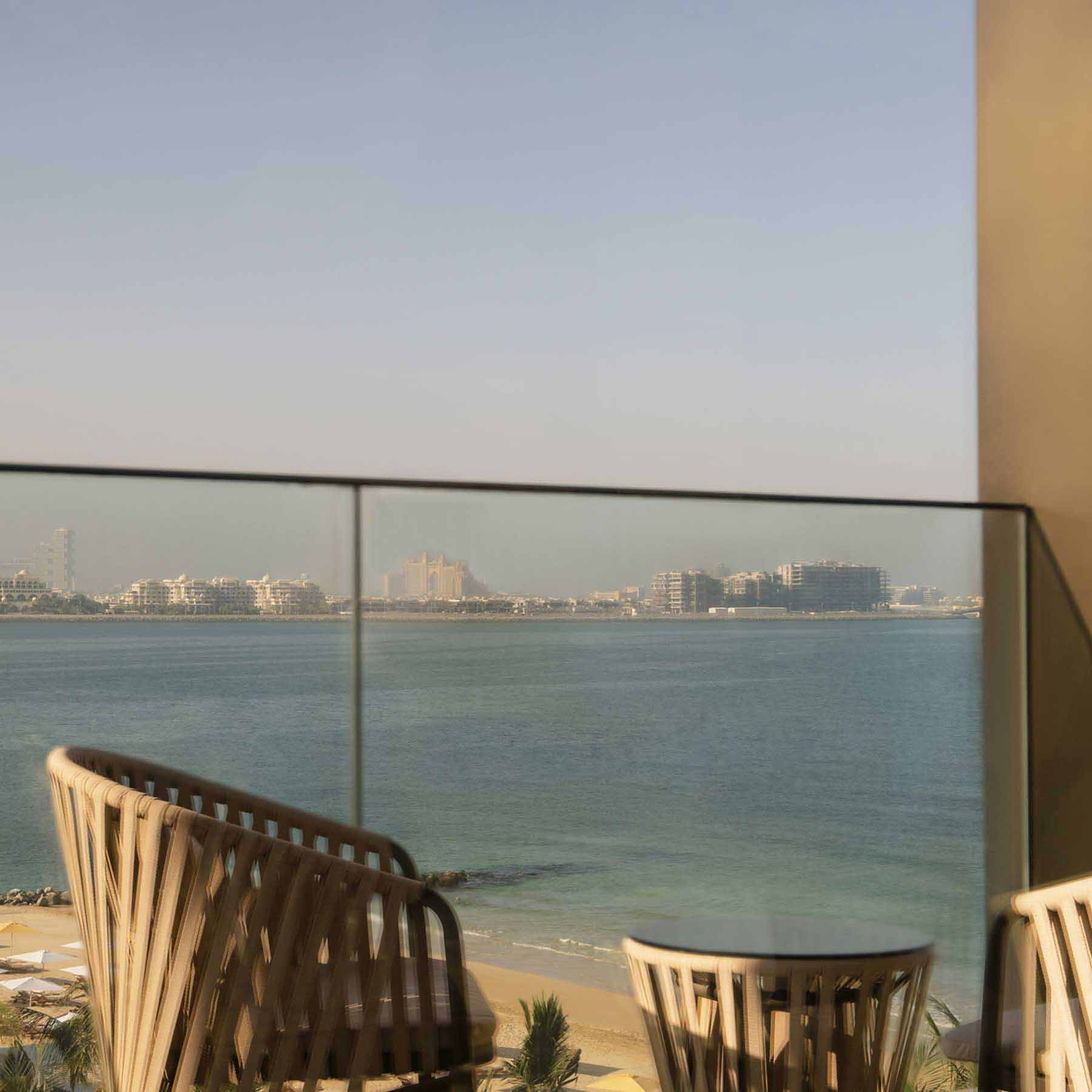 a balcony just off the guestroom with two chairs and side table with views of the sea
