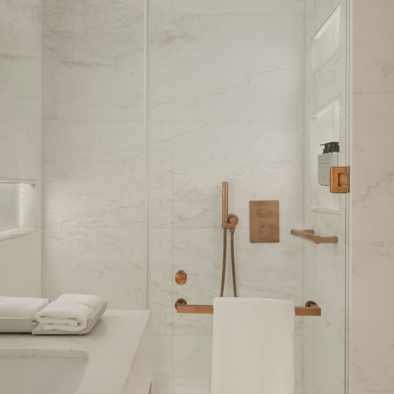 a white marble shower with a glass door and gold accents