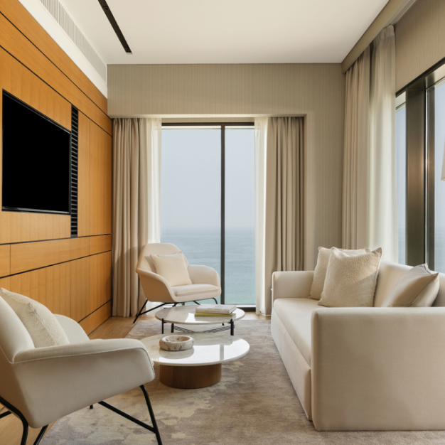 A cozy seating area features plush sofas and chairs, overlooking the ocean through large windows, inside a luxurious room at Delano Hotel, Dubai.