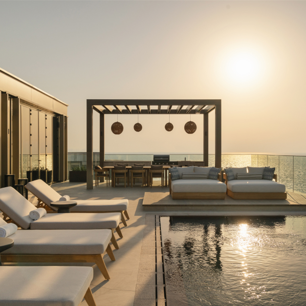 a pool at sunset with views of the sea and lounge seating