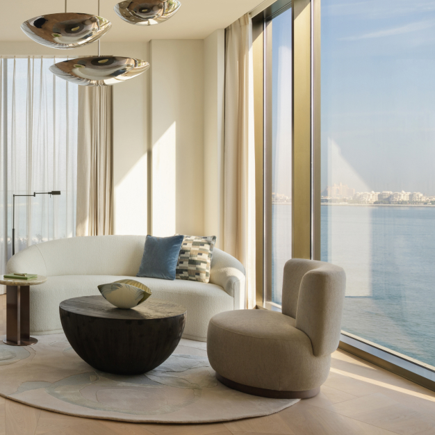 the second half of a bedroom with a seating are with a white couch and white chair around a round coffee table