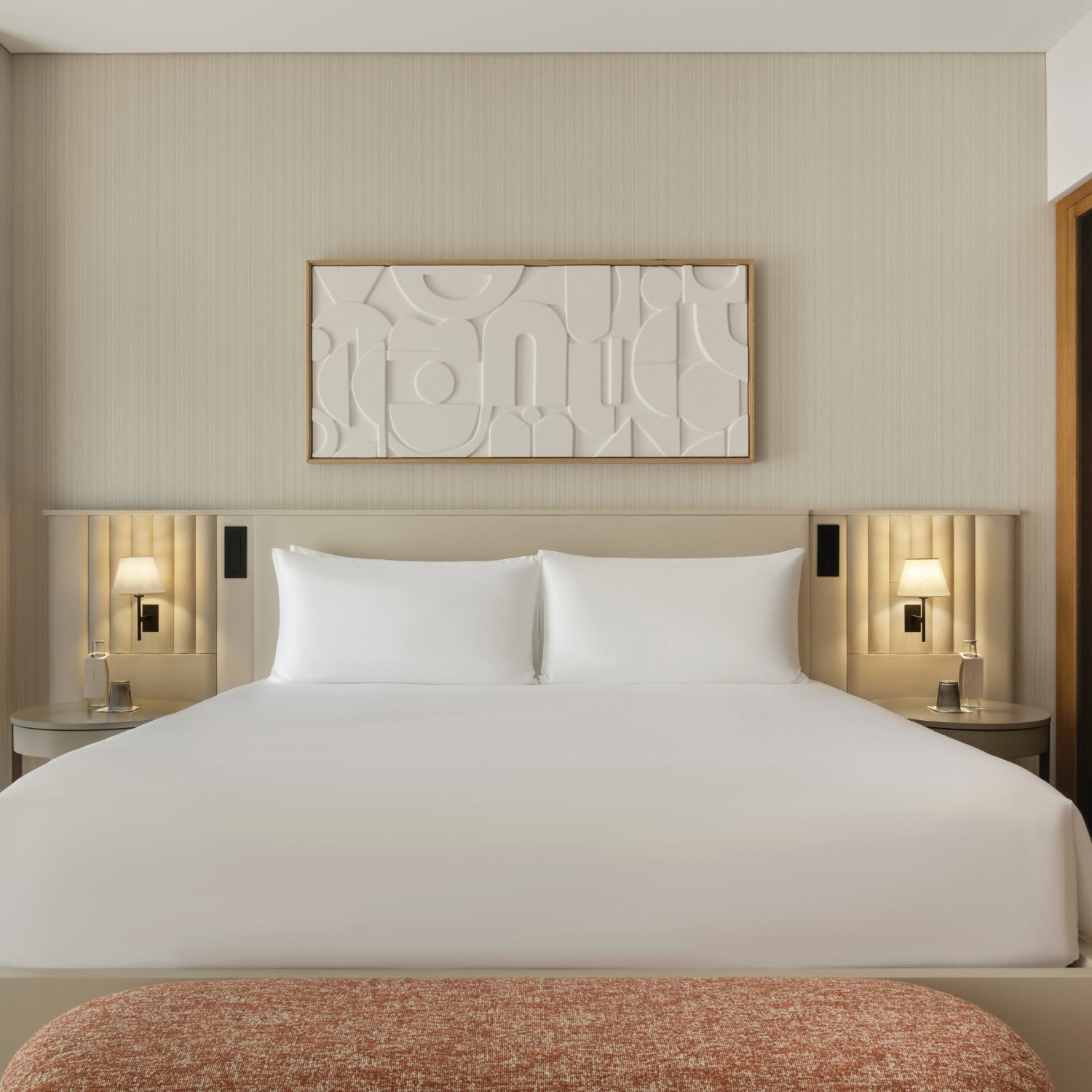 a front view of the bed with two sconces above the bedside tables and white canvas artwork above it