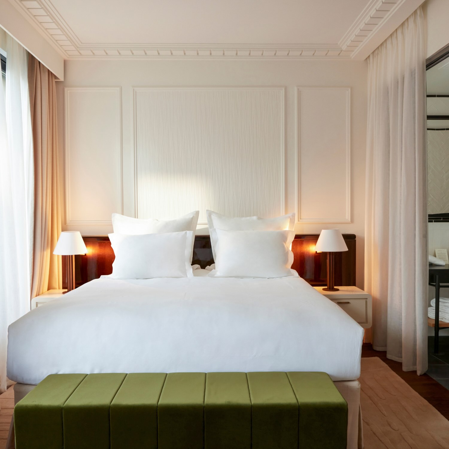 the front view of a bed with drapes over the windows, a green bench and bedside tables