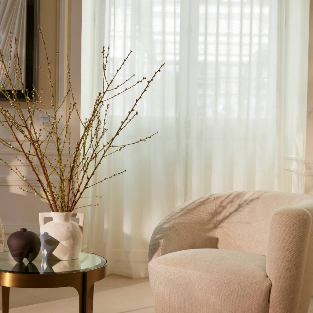 a white chair in front of a window with drapes and a small table