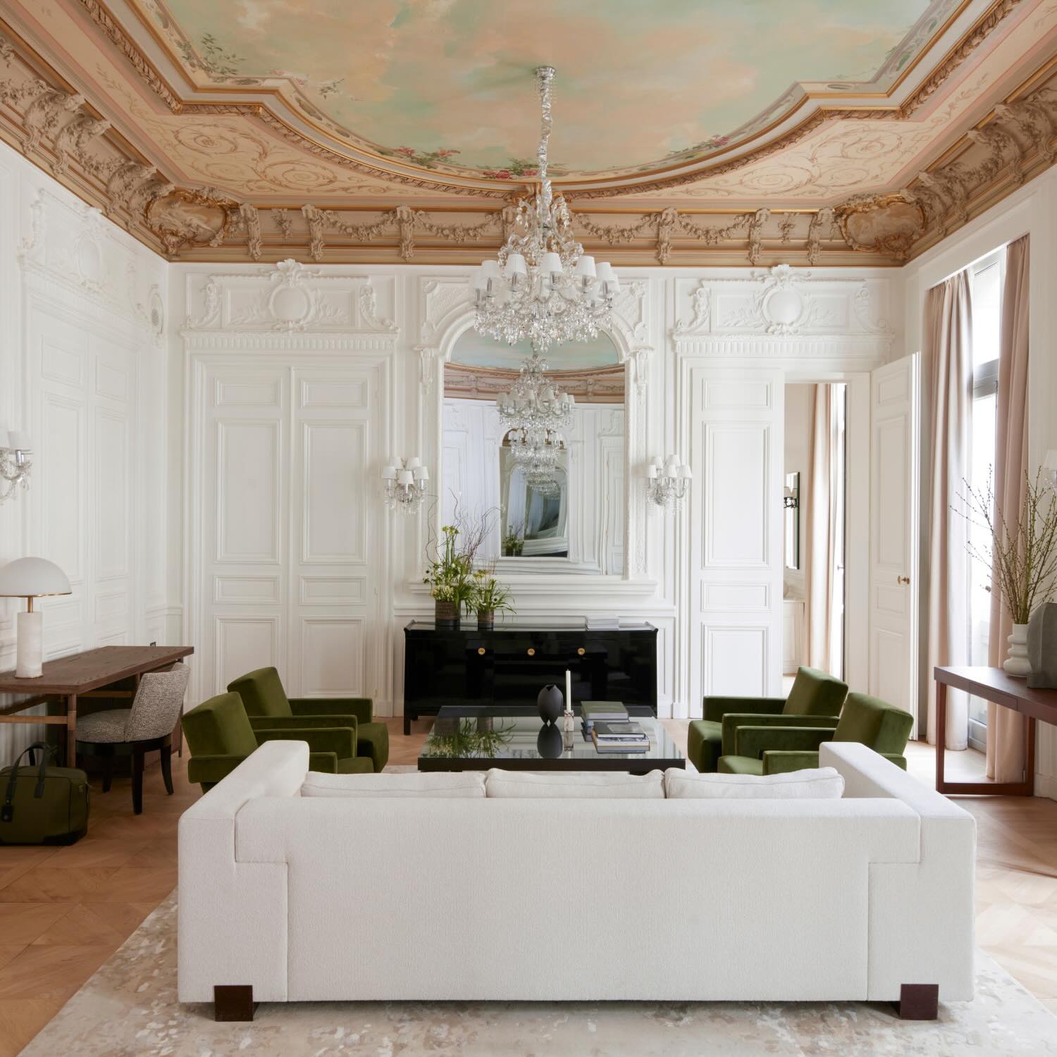 a suite living room with a grand glass chandelier and an ornate ceiling