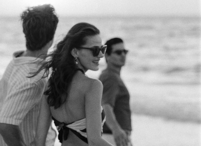 three people walking by the beach in black and white