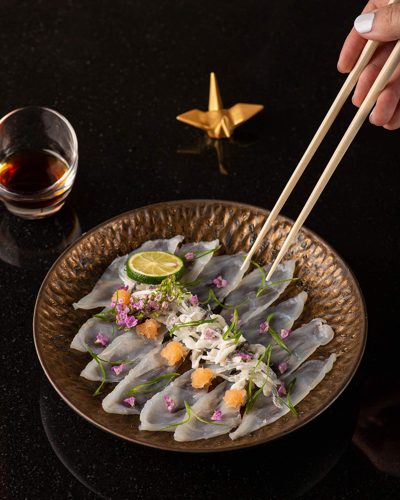 Un plat magnifiquement présenté, composé de tranches de sashimi disposées sur une assiette décorative, avec des baguettes tendues vers un morceau.