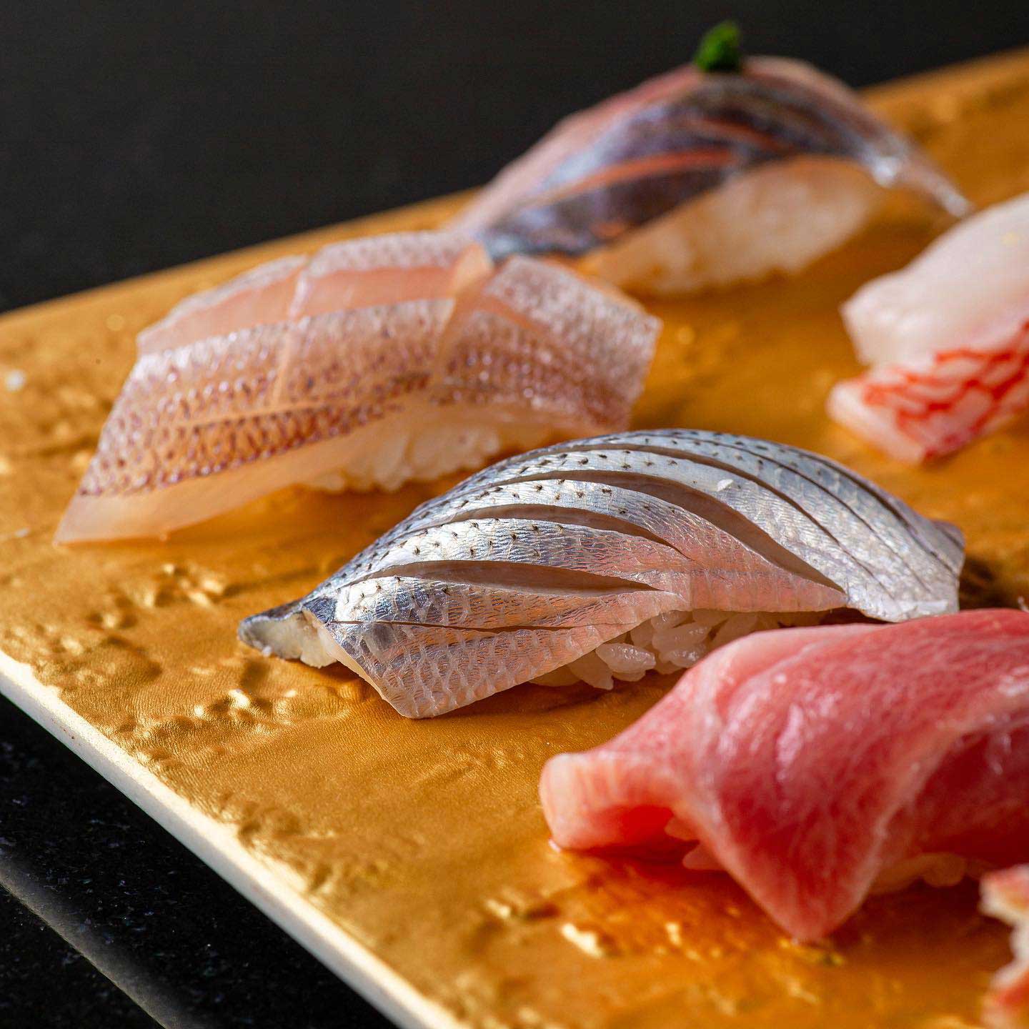 Close-up of a beautifully plated selection of sushi, featuring glistening cuts of fresh fish atop perfectly shaped rice, served on an elegant golden platter.