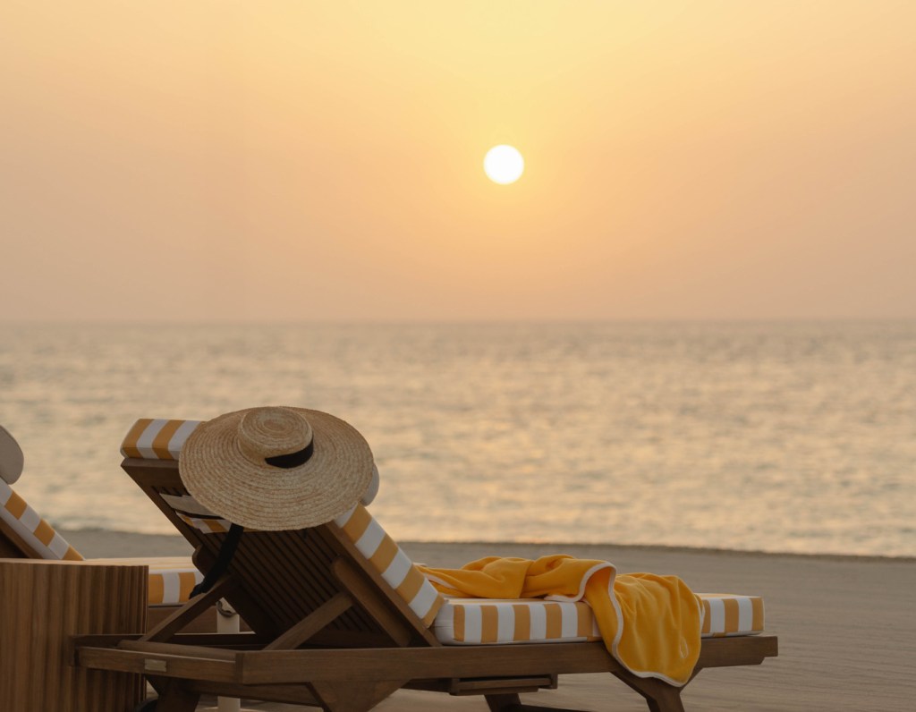A serene beach view at sunset with a lounge chair and striped towel facing the sea
