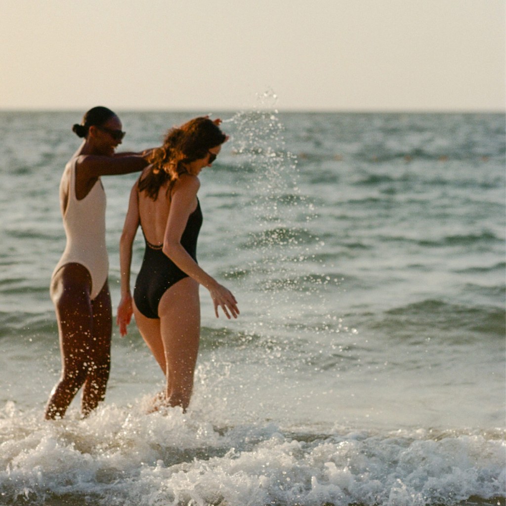 Two women walking along the shoreline, enjoying the ocean waves with a golden retriever dog beside them.