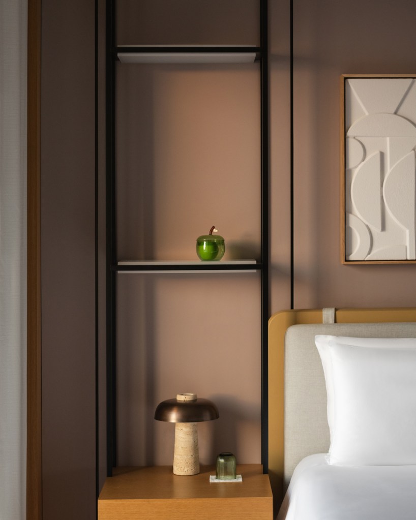 Stylish bedroom corner featuring a neatly designed shelf with a green decorative apple, a modern table lamp on a wooden nightstand, and abstract wall art, creating a warm and minimalistic aesthetic.