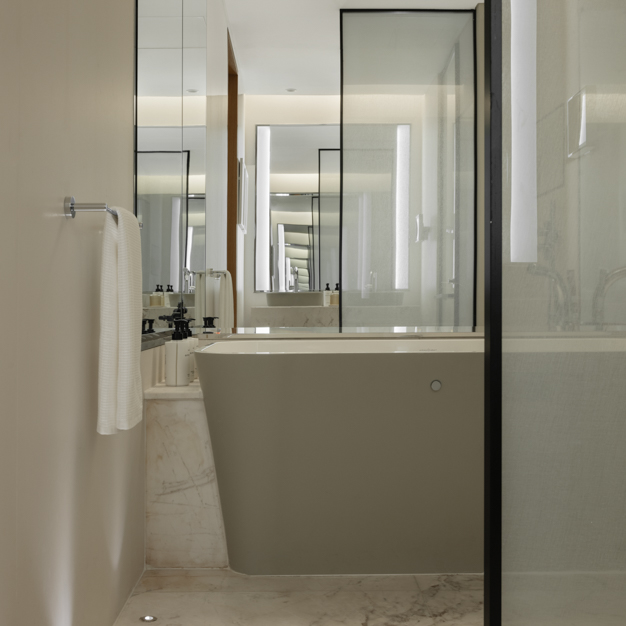 Modern bathroom featuring a sleek freestanding bathtub with a matte finish, marble flooring, and glass partitions. A towel hangs on a rail, and mirrored walls reflect the clean, minimalist design. Subtle lighting enhances the elegant, contemporary ambiance.