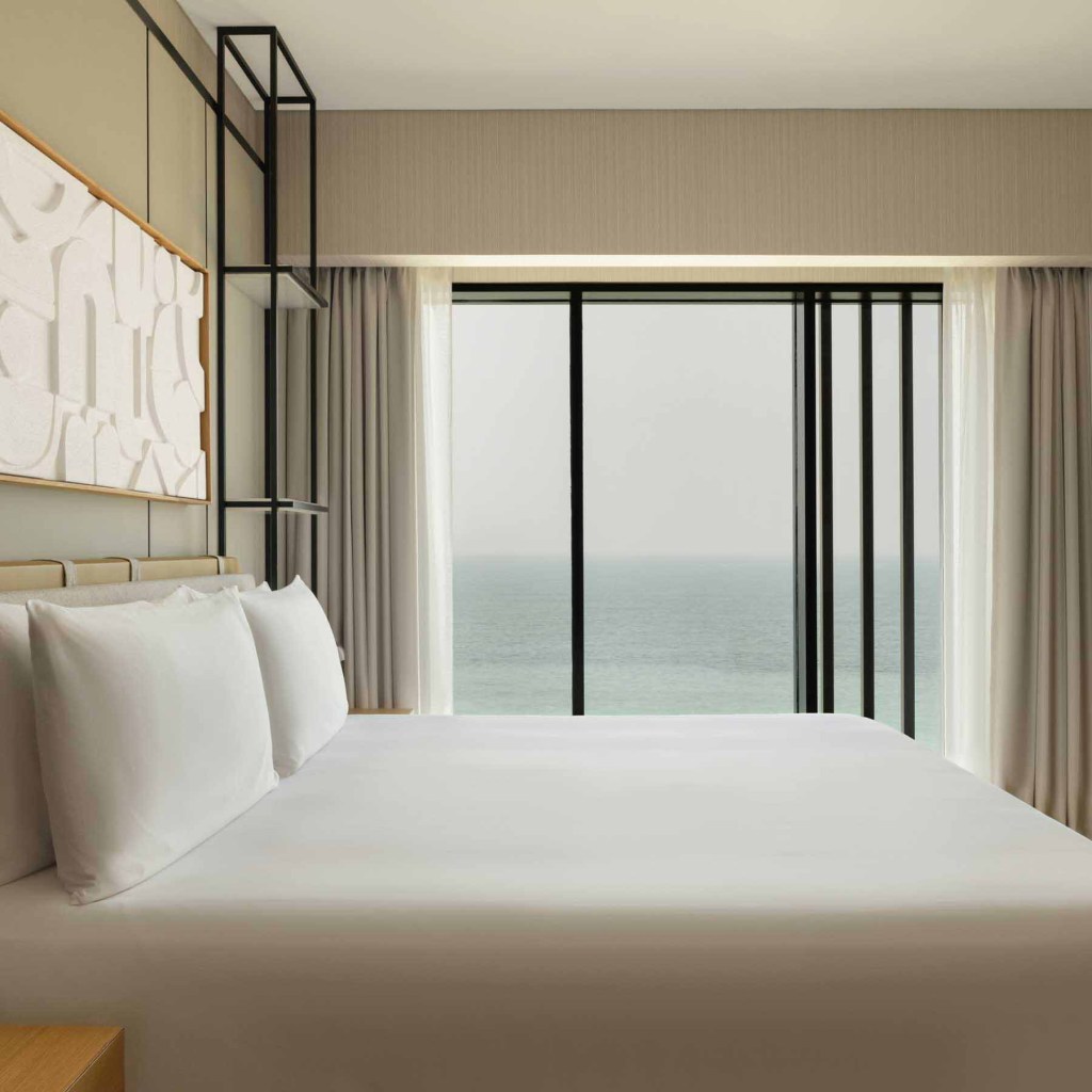 the side view of a king bed in a guestroom with views of the sea