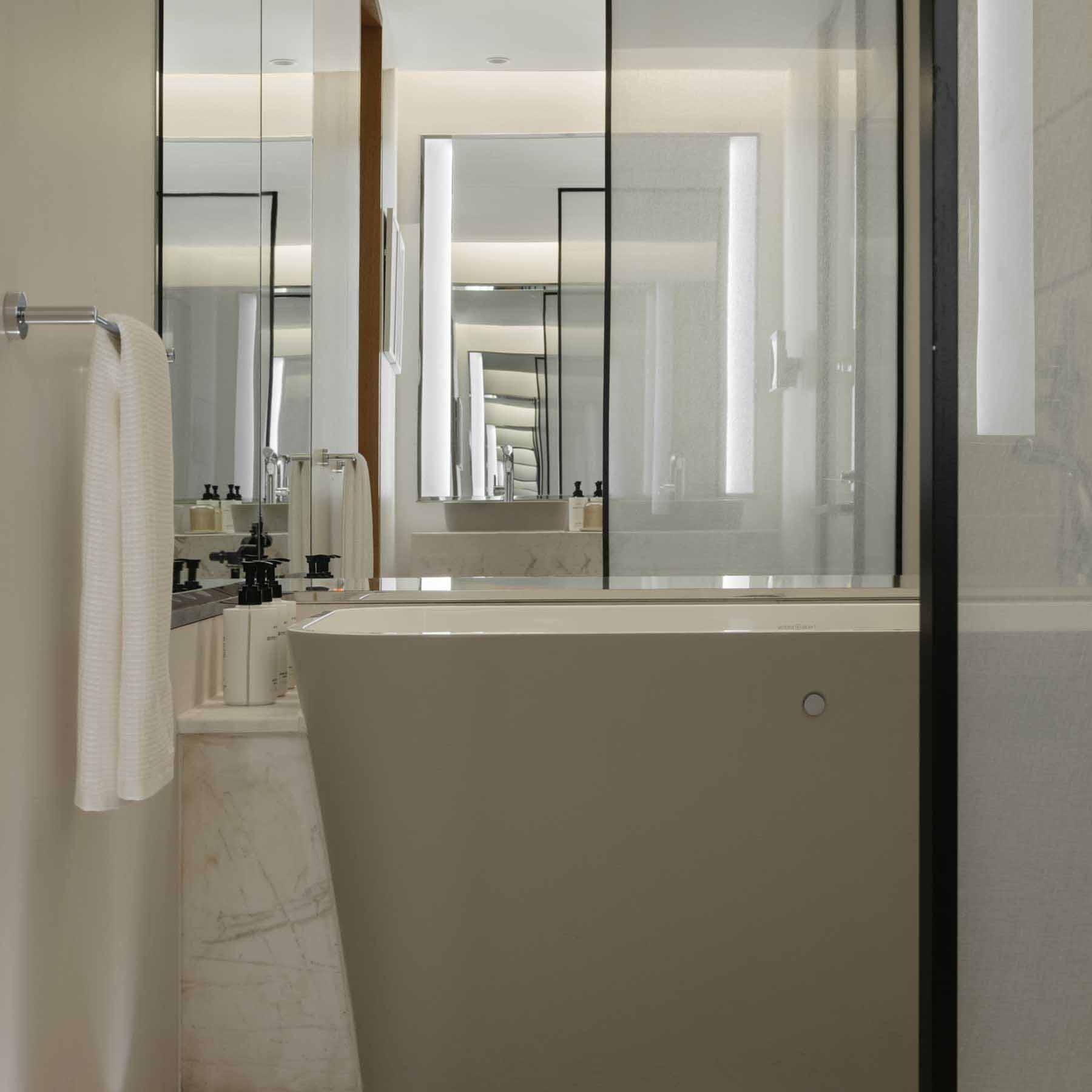 Modern bathroom featuring a freestanding matte-finish bathtub, marble flooring, and a glass-enclosed shower area. A towel hangs neatly on the wall, while large mirrors reflect the space, creating a bright and open atmosphere with sleek, minimalist design elements.