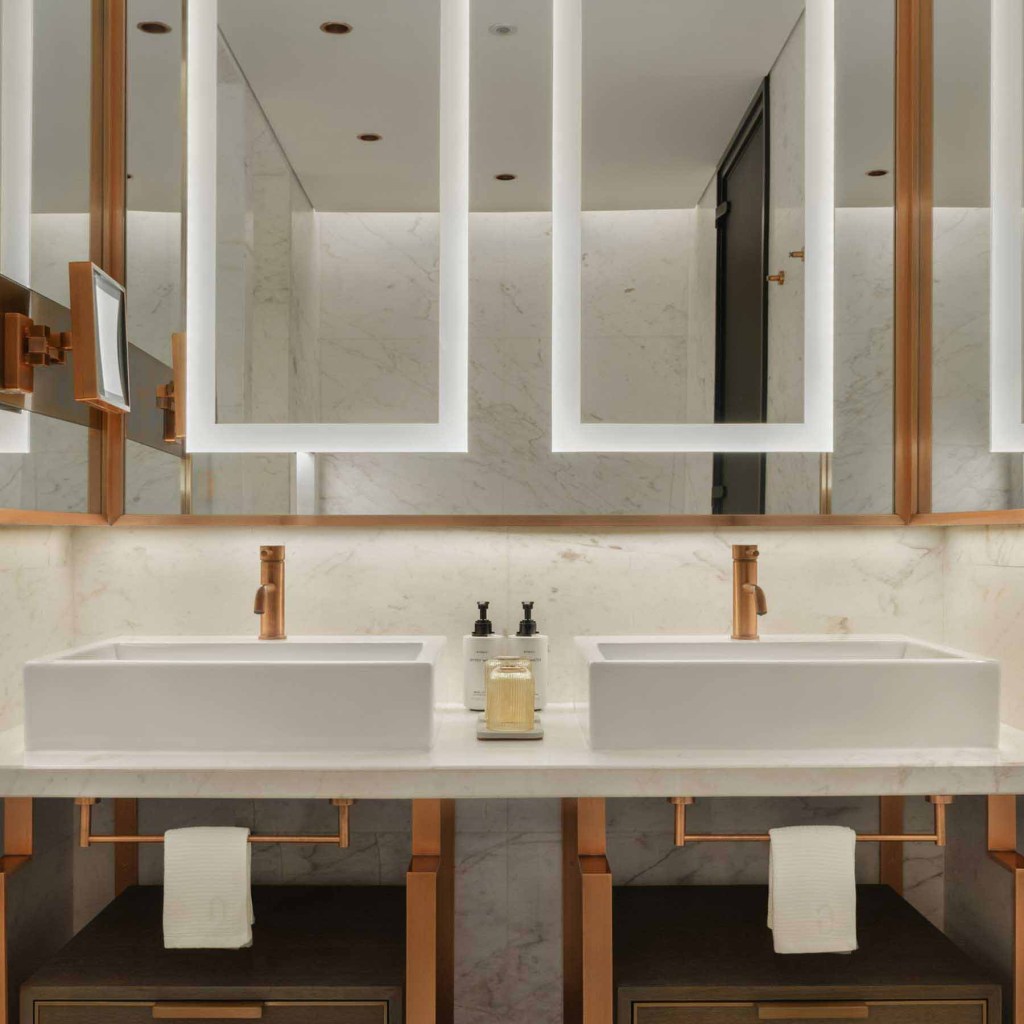 a white marble bathroom with a vanity that has two sinks and a large mirror