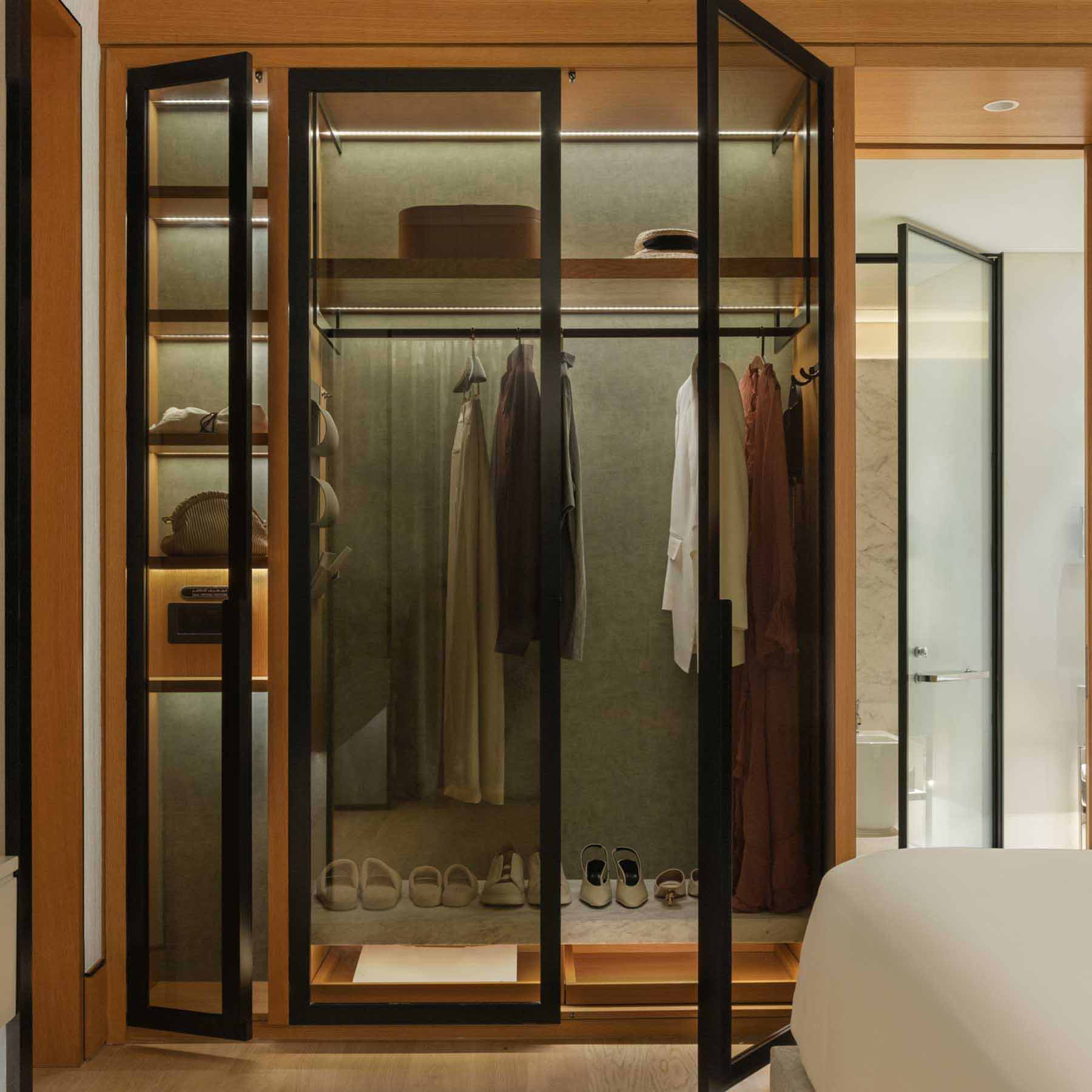 a built in armoire with clothes hanging and glass doors