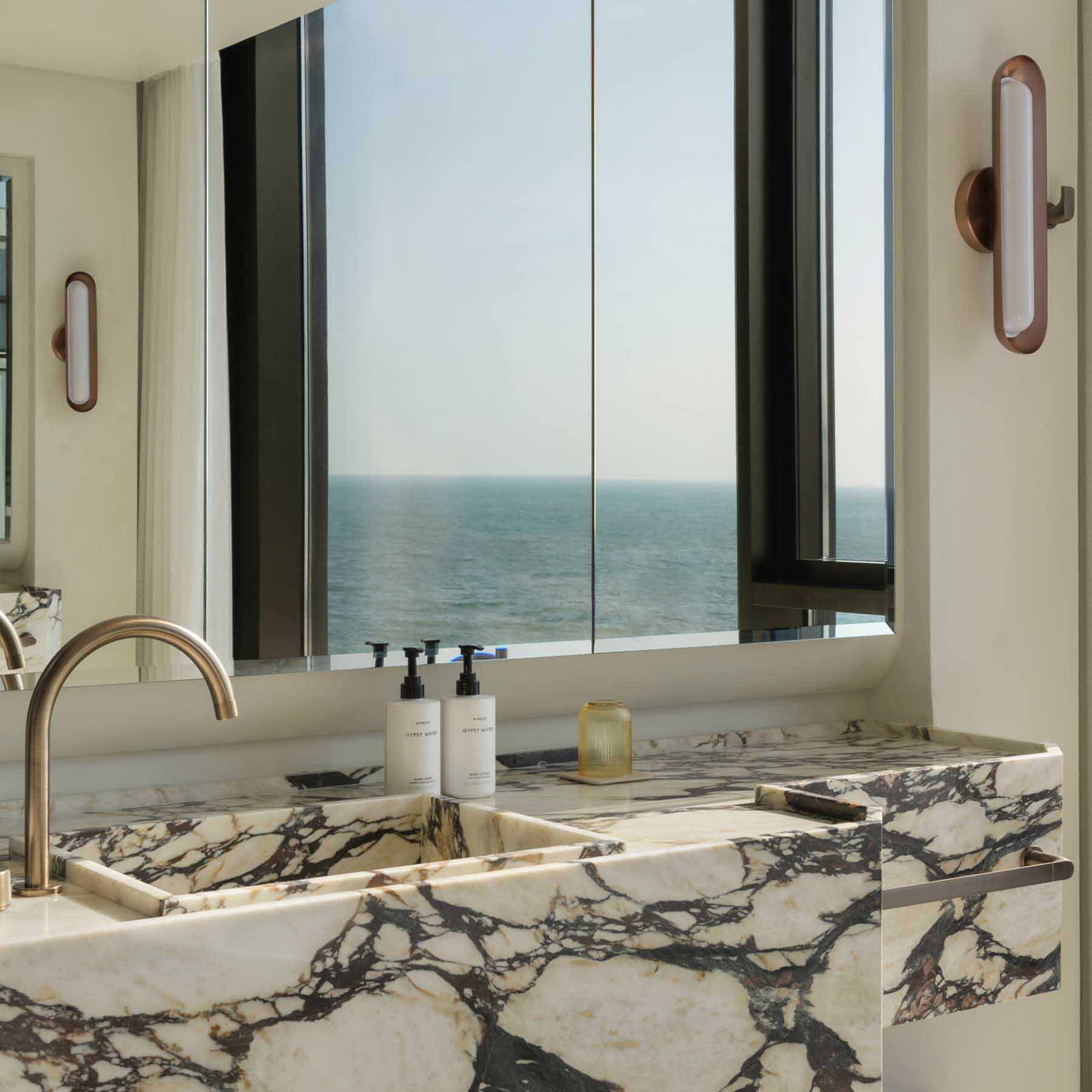 a luxurious bathroom with marble and floor to ceiling windows with views of the sea