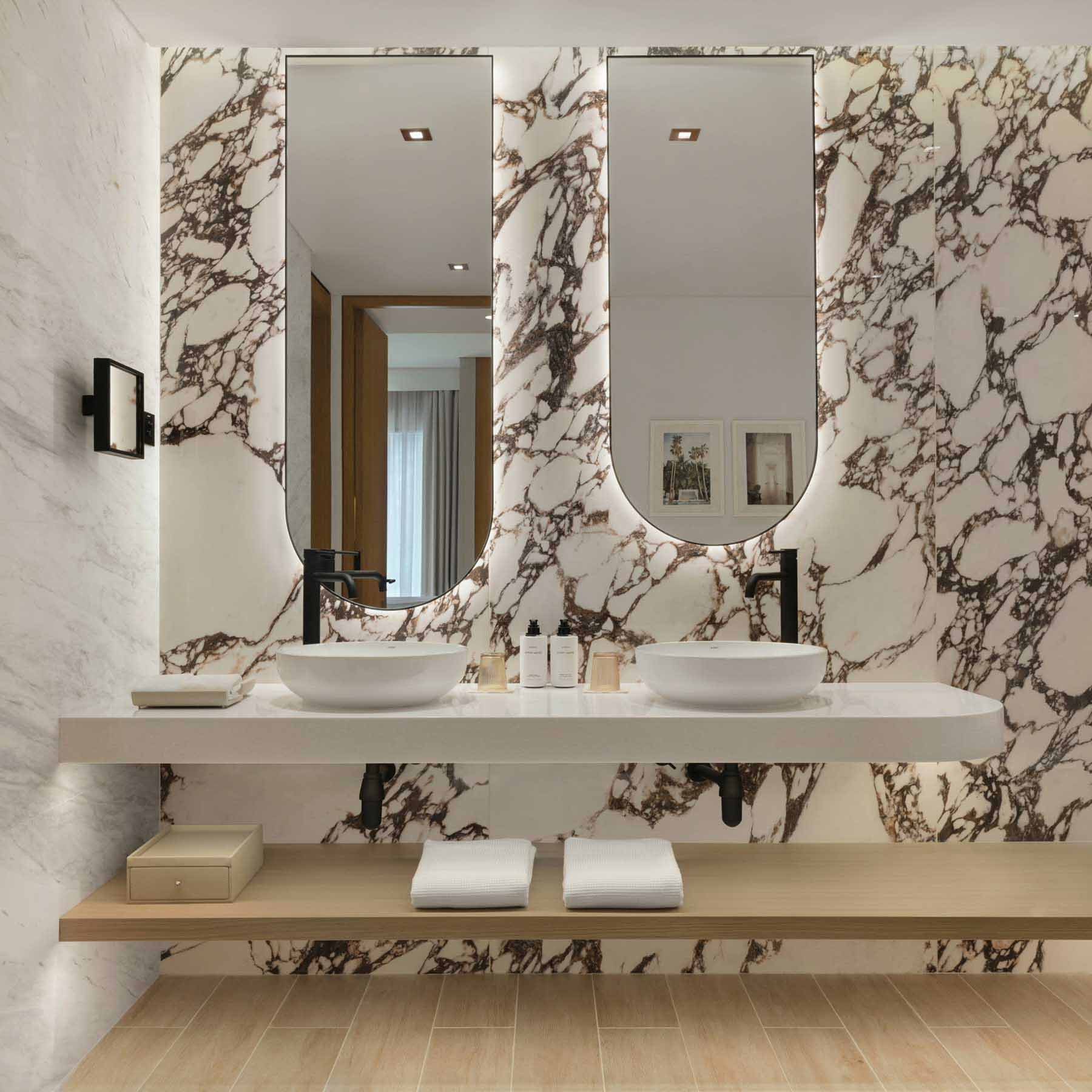 a luxurious marble bathroom with a double vanity and two oval shaped mirrors