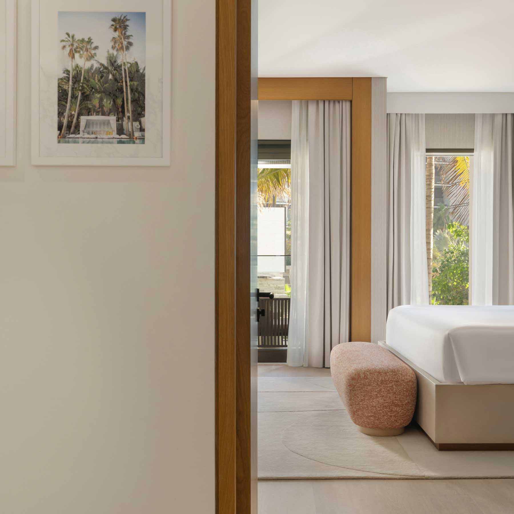 the view of the bedroom from the bathroom with the foot of the bed visible and the salmon colored bench