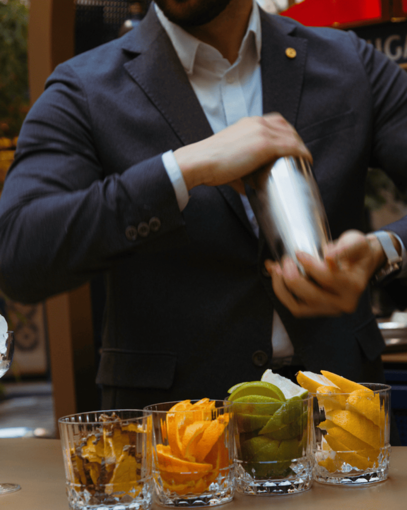 An elegantly dressed bartender behind the bar creating a cocktail with Brugal.