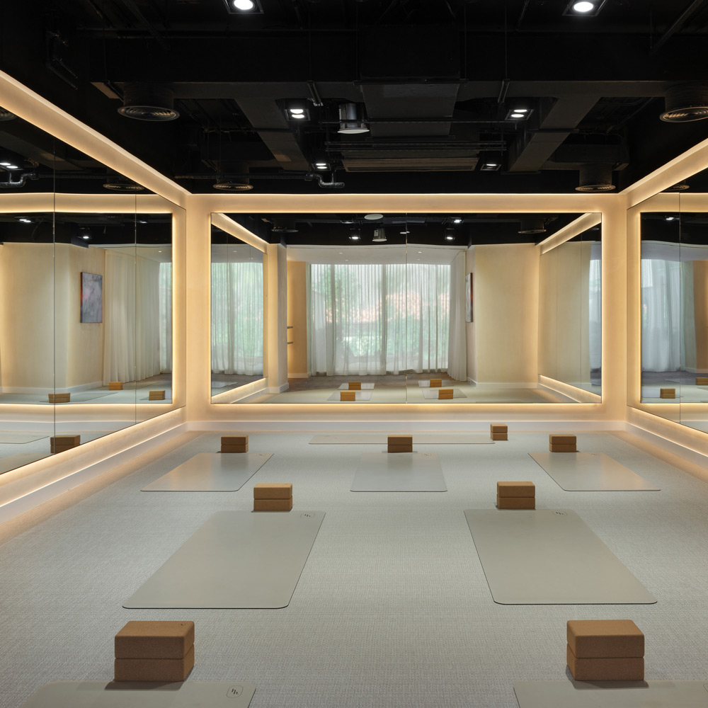 Modern, softly lit yoga studio with floor mats and blocks neatly arranged in a mirrored space, offering a serene and minimalist environment for wellness and meditation.