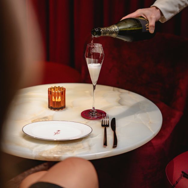 Close-up of champagne being poured into a flute glass on an elegant marble table with a candle, plate, and cutlery at Rose Bar, Delano Dubai.