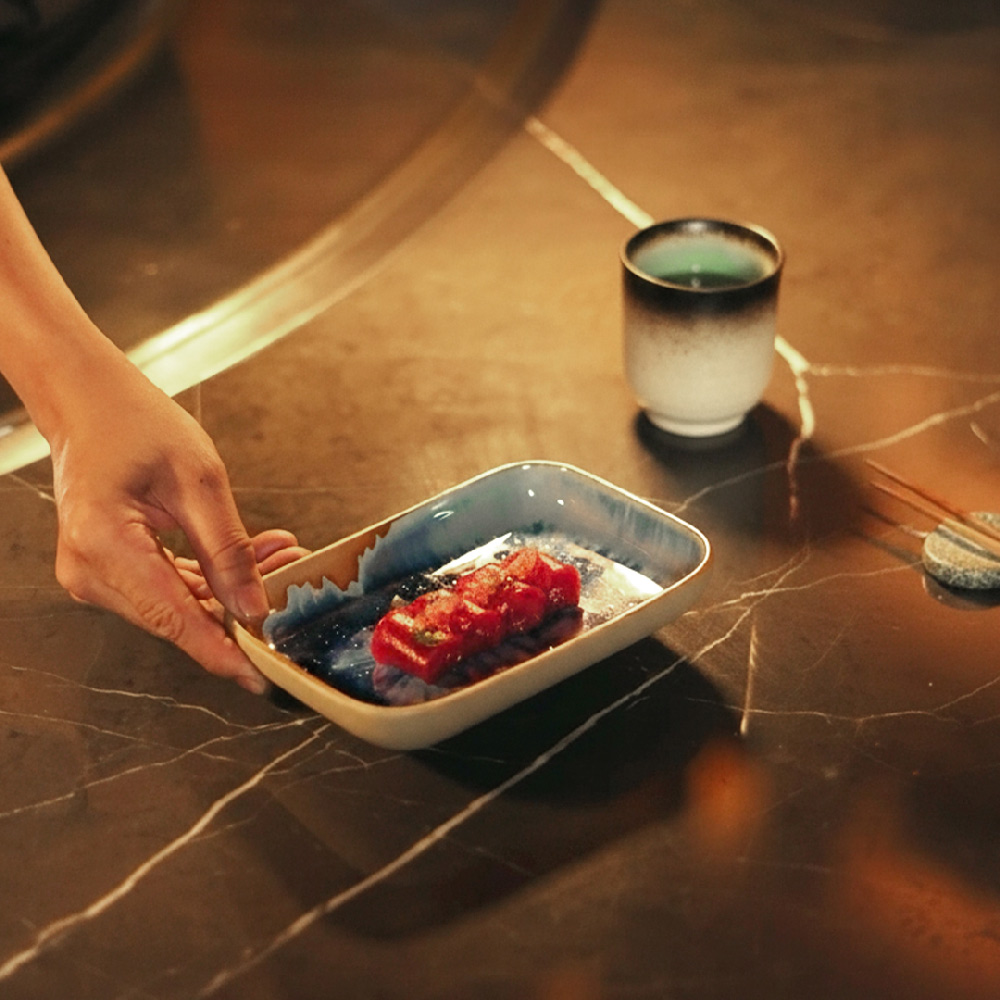 A chef places a beautifully presented Japanese dish on a marble counter at Teppanyaki: The Delano Way.