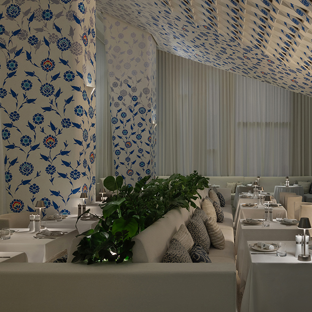 Elegant restaurant interior featuring blue floral patterned walls and ceiling, white table settings, soft ambient lighting, and lush greenery creating a refined and serene dining atmosphere.