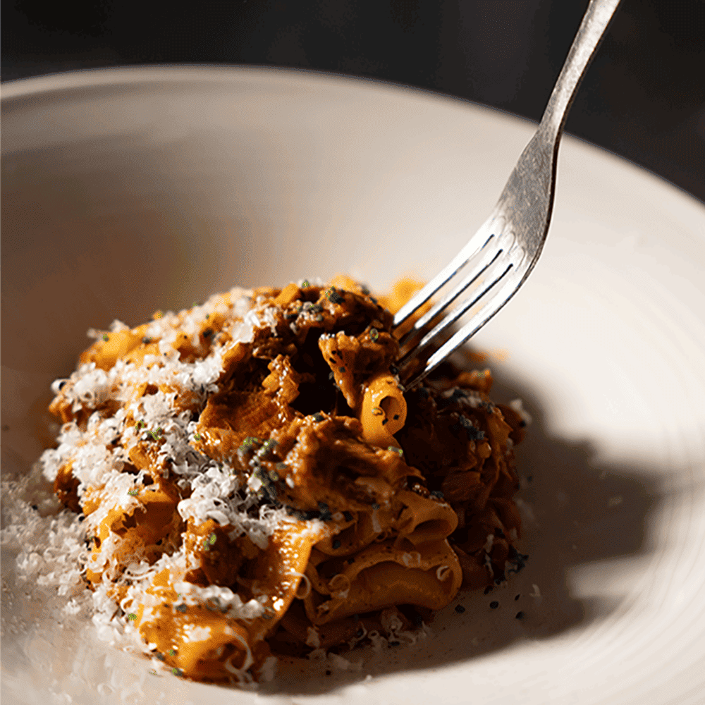 white plate with freshly made papardelle, a red sauce and a little bit of grated parmesan. We can see a fork on the left upper corner, as if someone is about to eat the plate, at Maison Delano Paris.