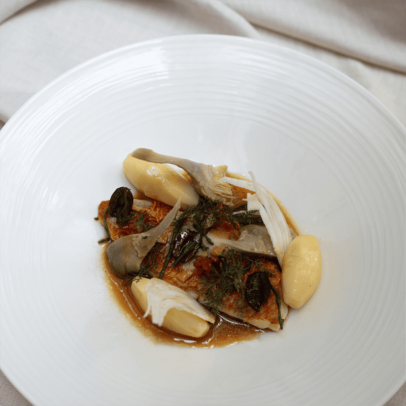 Focus on a red mullet dish with baby violet artichokes, new potatoes, saffron, rockfish juice, at Maison Delano Paris.